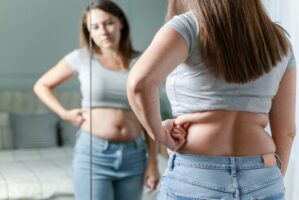 Woman standing in front of mirror looking at the stubborn fat around her waist.