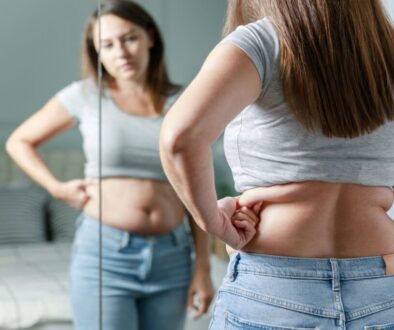 Woman standing in front of mirror looking at the stubborn fat around her waist.