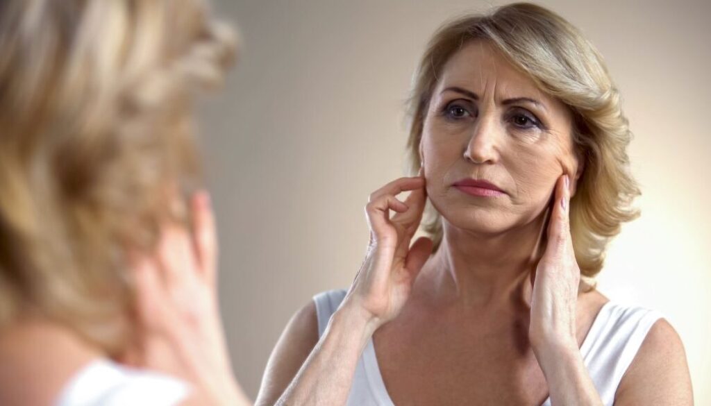 Woman looking in the mirror at the sagging skin on her face.