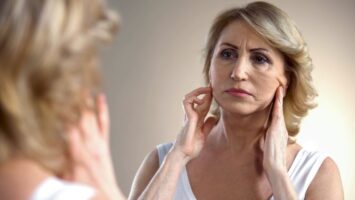 Woman looking in the mirror at the sagging skin on her face.
