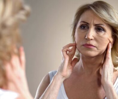 Woman looking in the mirror at the sagging skin on her face.